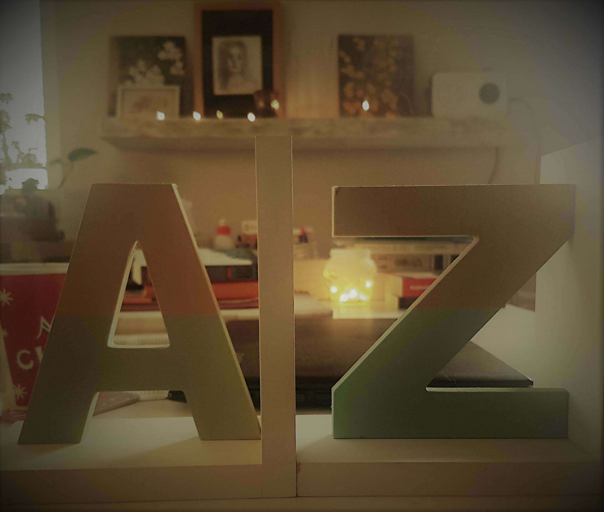 Drewniane literki A i Z, symbolizujące alfabet Oli, z tyłu cały zabałaganiony stól - książki, kawa, lampki, obrazki