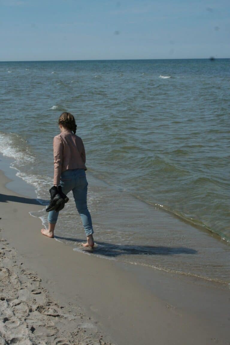 dziewczyna idąca brzegiem morza, w ręku trzyma buty i idzie boso