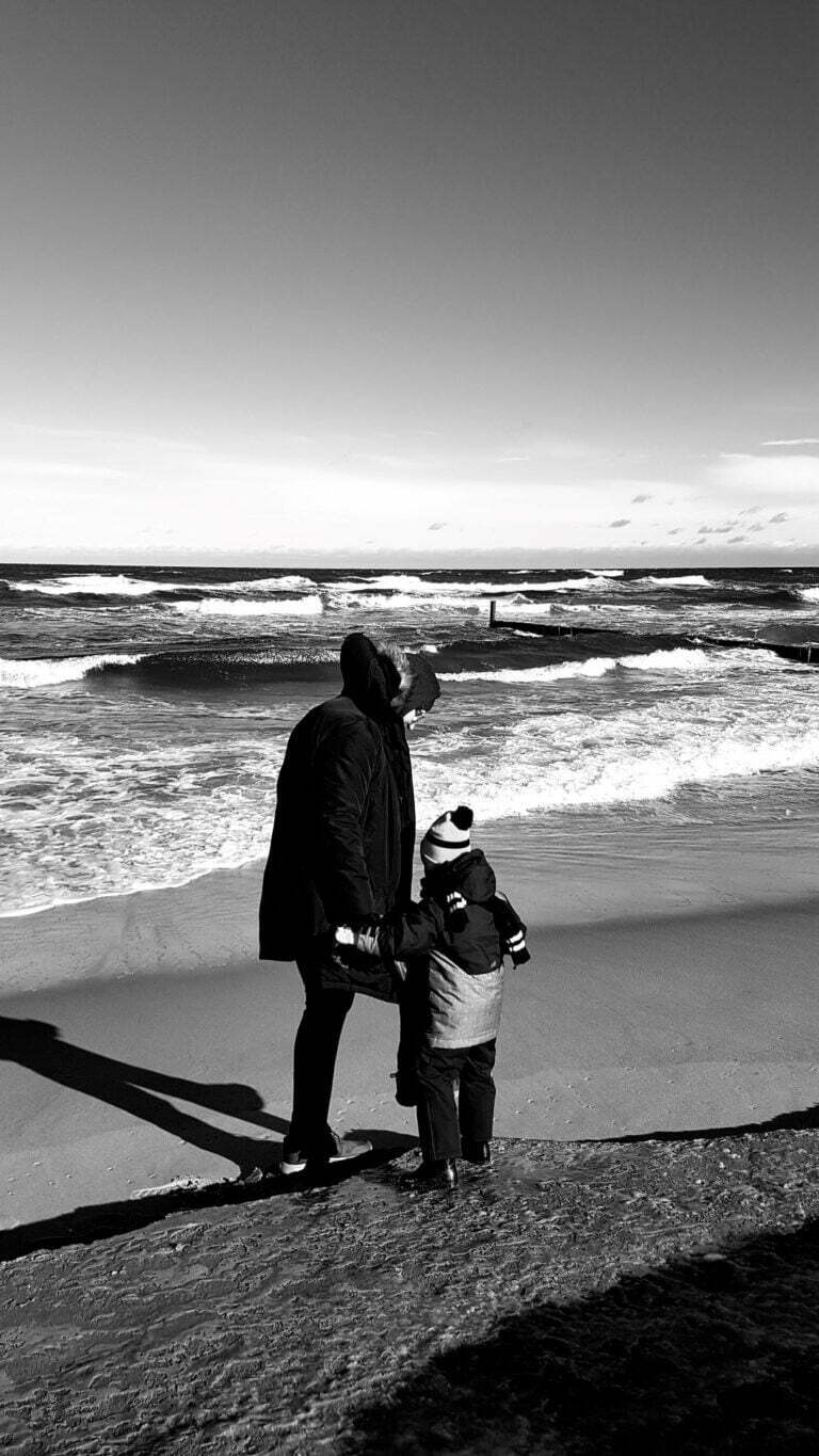 czarno - białe zdjęcie and morza, tata idzie brzegiem plaży z synkiem