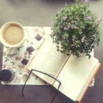 otwarta książka, obok kawa, czekoladki i kwiatki
