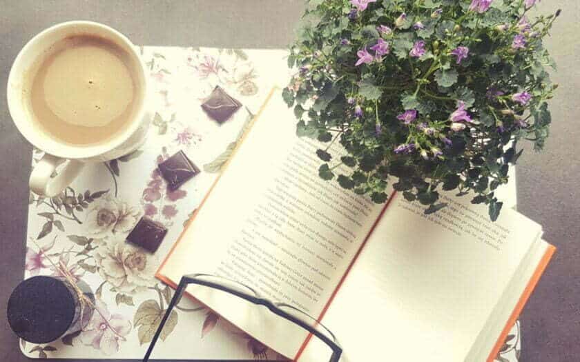 otwarta książka, obok kawa, czekoladki i kwiatki