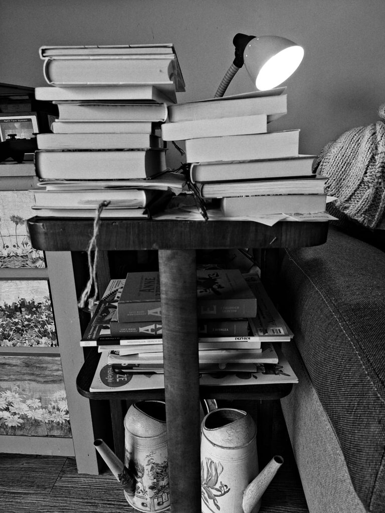 książki ułożone na nocnym stoliku, oświetlone nocną lampką